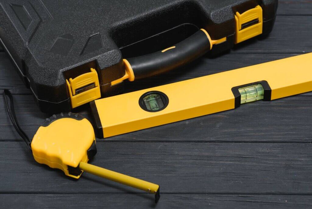 black toolbox, tape measure, and level on black wood background