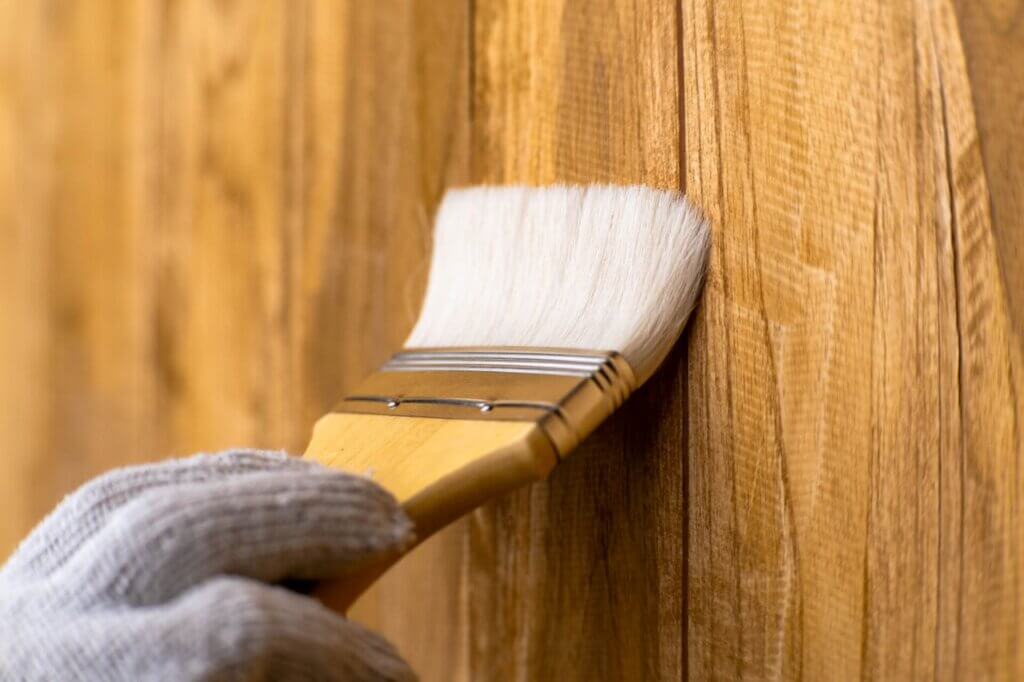 hand holding a brush staining a wooden fence