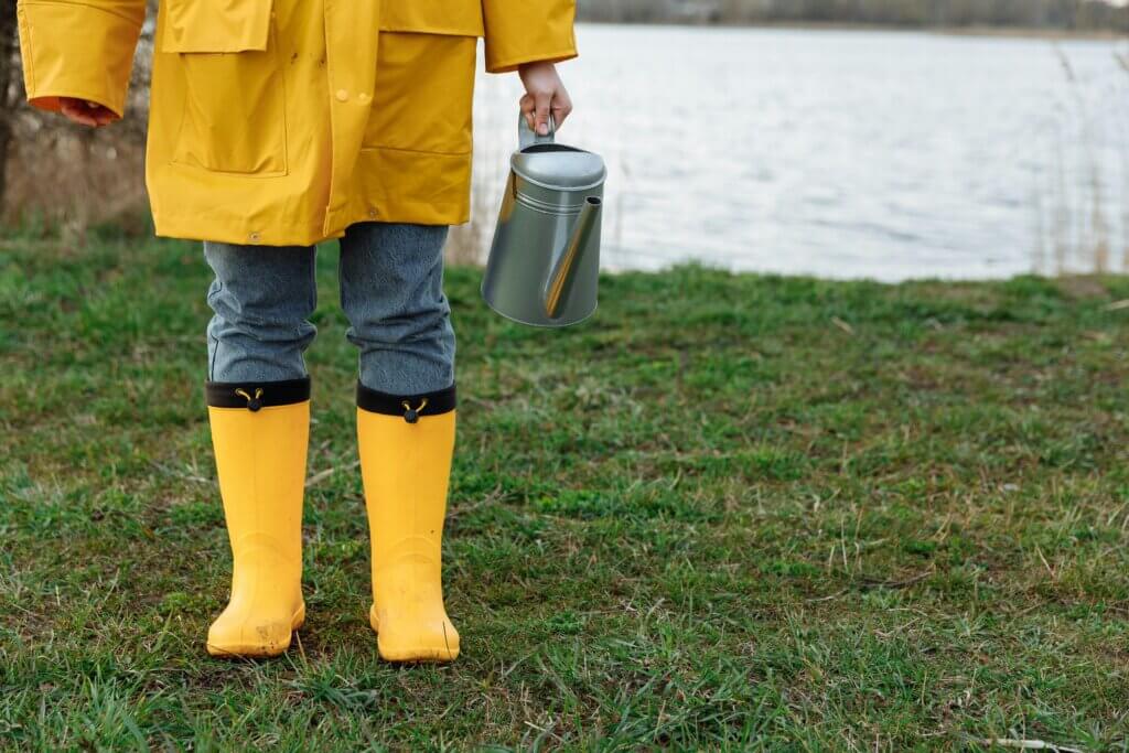 person holding a watering can wearing yellow coat and wellies