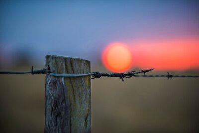 a wooden fence post with barbed wire and sunset in the background