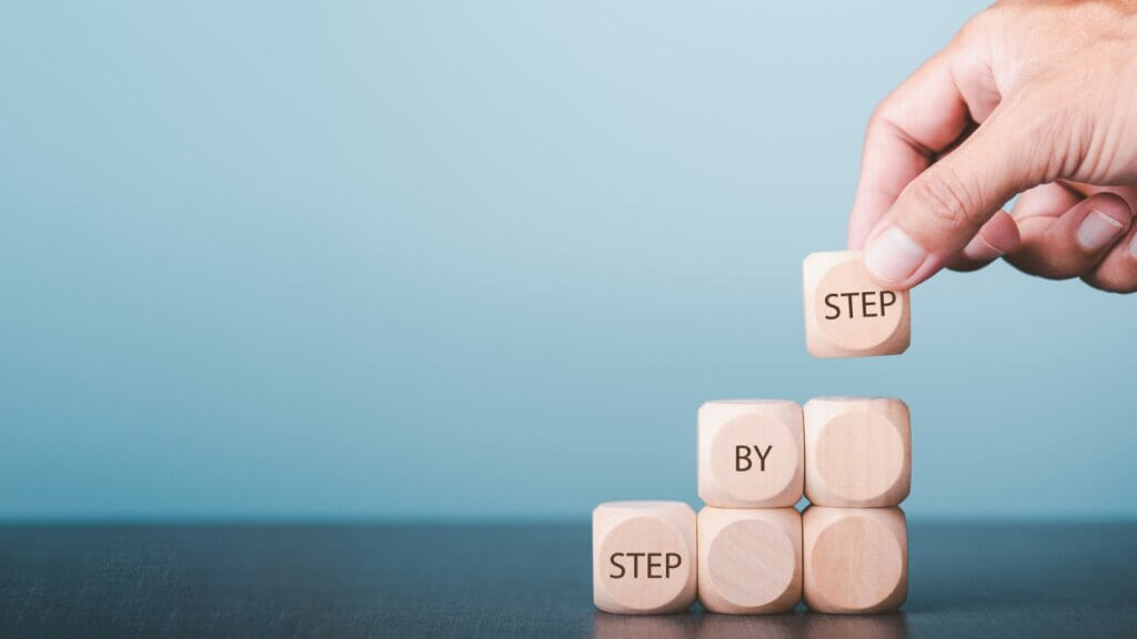 Hands arrange wooden blocks stacked into steps and display messages Step By Step