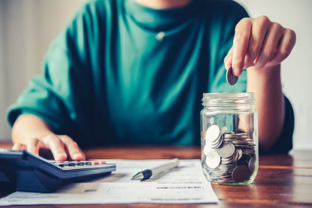 person using a calculator while putting coins in a jar